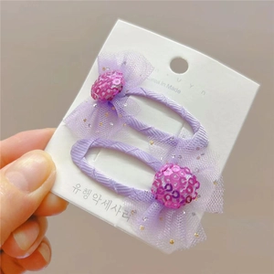 Détail de deux pinces à cheveux violettes à paillettes sur carton blanc à la main