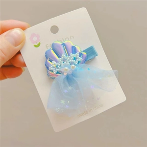 Macro detail of blue laser shell hair clip with pearls and mesh star bow on card