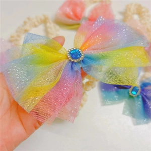 Close-up of rainbow gradient mesh bow headband with central blue gemstone and rhinestones