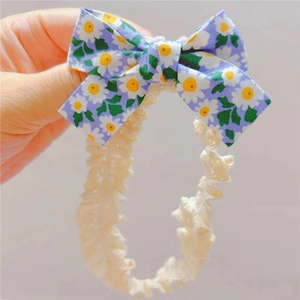 Détail d'un bandeau en dentelle pour bébé avec un nœud violet à imprimé marguerites