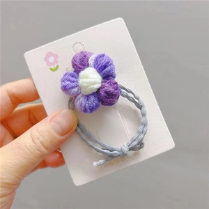 Detail eines handgefertigten Häkelblumen-Haargummis mit lila Strickblüten auf Karte