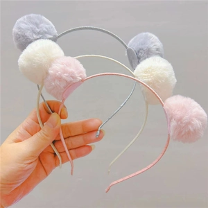 Détail de bandeaux à pompons en peluche gris, crème et rose avec des textures douces