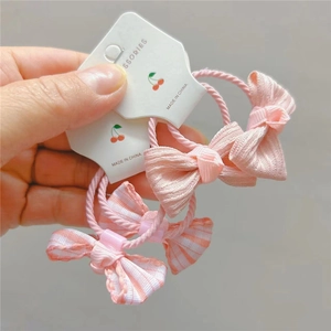 Dettaglio di elastici per capelli rosa con fiocco a scacchi e nastro a pieghe su carta