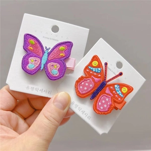 Détail de barrettes papillon brodées en violet et rouge avec texture de tissu fine