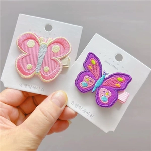Détail de barrettes papillon brodées rose et violet avec des bases enveloppées de tissu