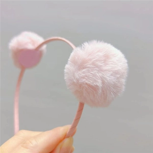 Gros plan d'un serre-tête en peluche rose clair avec pompons doux pour filles