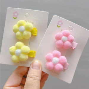 Close-up of plush flower hair clips in pink and yellow set on white display card