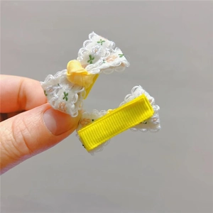 Dettaglio di due fiocchi in pizzo floreale con clip di sicurezza avvolte in nastro giallo