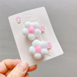 Close-up of two plush flower hair clips with pink and white pompoms on fashion card