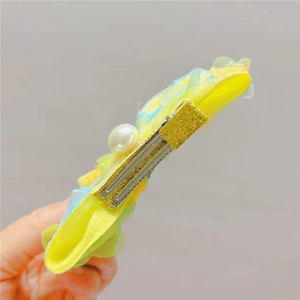 Détail rapproché de la barrette en maille jaune et bleue avec perle et fini pailleté doré
