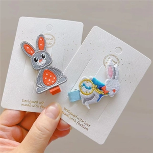 Detail of two handmade embroidered rabbit hair clips with fine needlework and duckbill clips