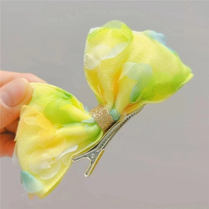 Détail d'un nœud à cheveux en tulle jaune et vert avec une pince à bec de canard en métal