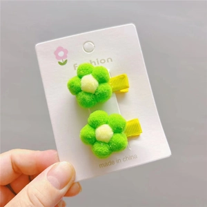 Close-up of two green plush flower hair clips with yellow centers and ribbon-wrapped bases