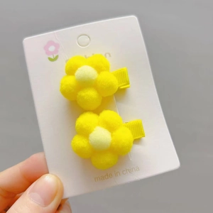 Detail of yellow plush flower hair clips with soft pompom texture and ribbon covered base