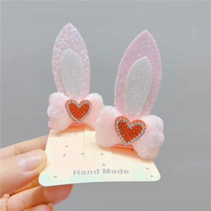 Pair of pink plush bunny ear hair clips with glitter bows and red heart rhinestones