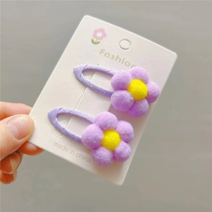 Close-up of plush purple flower hair clips with yellow center on display card