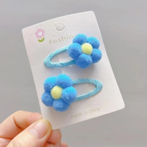 Detail of two light blue plush flower hair clips with yellow center pom poms for girls