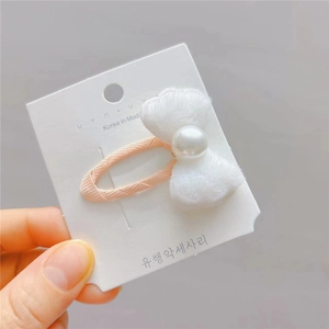 Détail d'une pince à cheveux avec nœud en fausse fourrure blanche et perle centrale