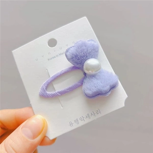 Vue détaillée d'une pince à cheveux nœud en peluche violette avec perle sur carton
