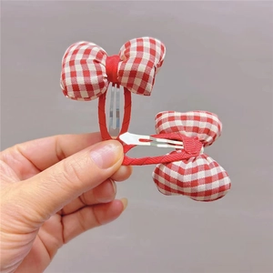 Detail showing a pair of red and white plaid bow hair clips held by hand for child style