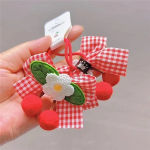 Detail of red gingham bow hair ties featuring knit flowers and cherry pom-pom charms