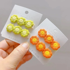 Detail of sweet hand-knitted flower hair clips in green and orange on display card