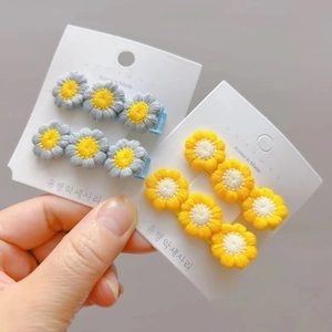 Detailed close-up of embroidered daisy hair clips in soft yellow and grey tones