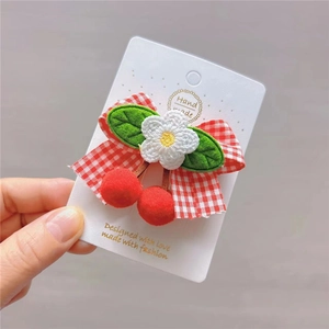 Detail of red plaid bow hair clip with floral embroidery and cherry pom-poms