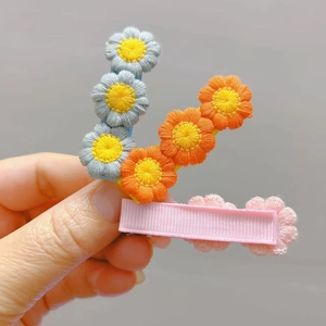 Close-up of three crochet flower hair clips in blue, orange, and pink for girls