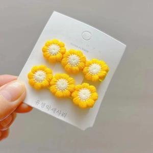 Macro detail of two yellow knitted daisy hair clips on white card for girls