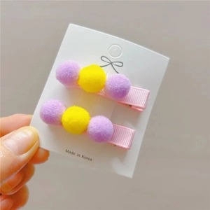 Detail of cute children hair clips with pink ribbon and colorful plush balls on a white card
