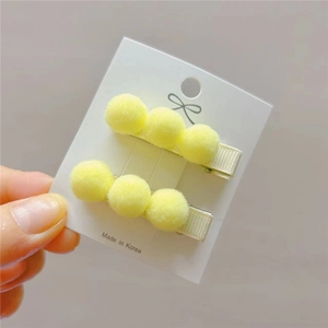 Detail view of yellow plush pom pom hair clips for girls on a white display card