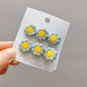 Close-up of dual grey and yellow embroidered daisy flower hair clips on a light blue base
