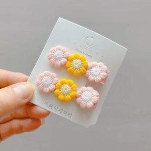Detail of handmade crochet flower hair clips in pink and yellow on a display card