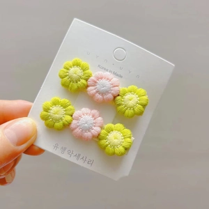 Detail showing two crochet daisy hair clips in pastel pink and green on a display card