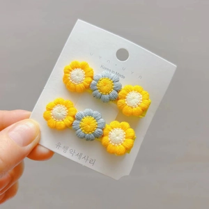 Close-up of knit daisy flower hair clips in yellow and white on a display card