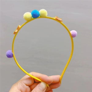 Détail d'un serre-tête jaune orné de pompons en peluche colorés et d'étoiles en feutrine
