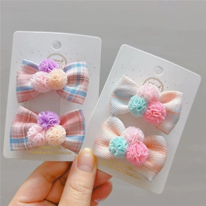 Dettaglio di fermagli per capelli in tessuto a scacchi con pompon colorati su cartoncino