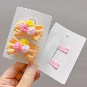 Dettaglio dei fermagli per capelli a quadretti rosa e gialli con pompon su carta