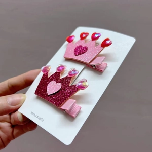 Detailed view of two glittery heart crown hair clips in pink and rose red tones