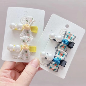 Detail view of handmade floral bow hair clips with pearls on a white display card