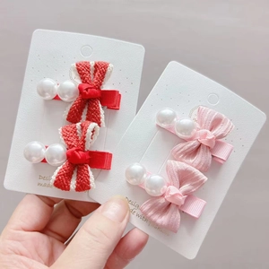 Detailed view of handmade bow hair clips with pearls in red stripes and soft pink fabric