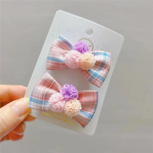 Dettaglio di fermagli per capelli a quadretti per bambina con pompon colorati su carta