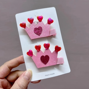 Detailed macro view of two pink glitter crown hair clips with heart shaped gemstones