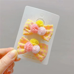 Dettaglio di fermagli per capelli a quadretti con pompon colorati su scheda di supporto