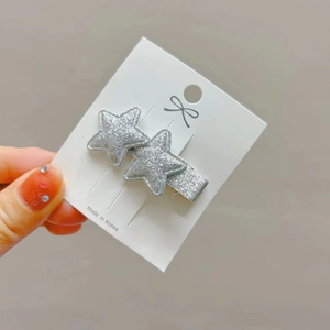 Detailed view of silver glitter star hair clips on a white display card accessory