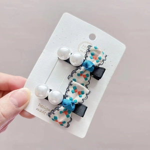 Floral bow and pearl hair clips set for girls on a white card display in hand