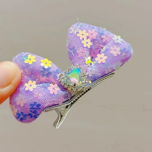 Detail of sequin bow hair clip featuring a purple mesh and heart-shaped colorful rhinestone