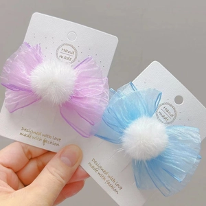 Detalle de pinzas para el cabello con lazo de malla azul y púrpura con pompones de piel blanca