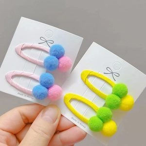 Close-up of colorful plush pom-pom hair clips for girls on a white display card